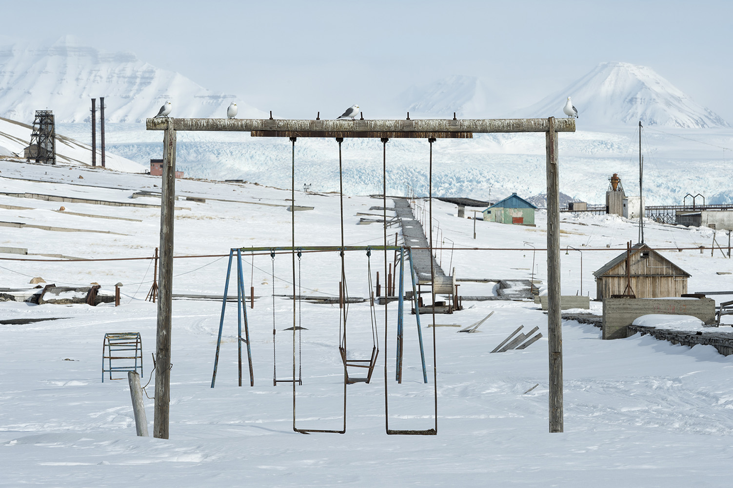 Birds sitting on the swing in the deserted playground at Pyramiden.Pyramiden is a Russian settlement and coal mining community on the archipelago of Svalbard, Norway. Founded by Sweden in 1910 and sold to the Soviet Union in 1927, Pyramiden was closed in 1998 and has since remained largely abandoned with most of its infrastructure and buildings still in place.